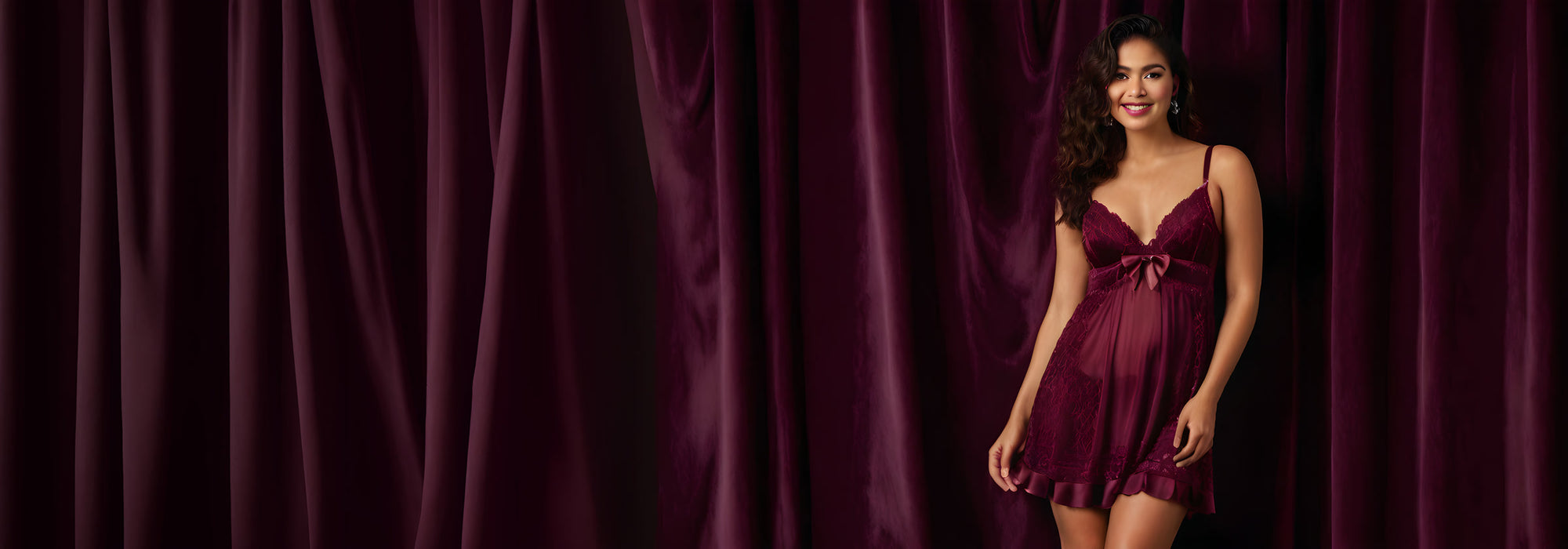 Model in a burgundy lace babydoll with a satin bow and sheer chiffon skirt against plum velvet curtains